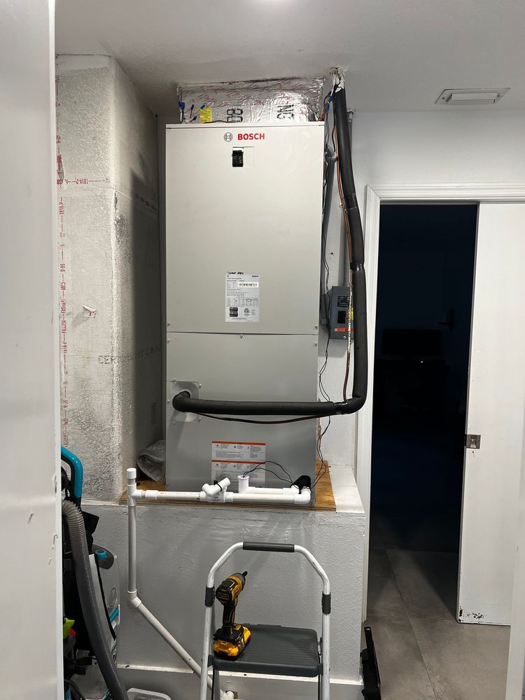 A white HVAC unit installed in a closet-like space with pipes and tools visible.