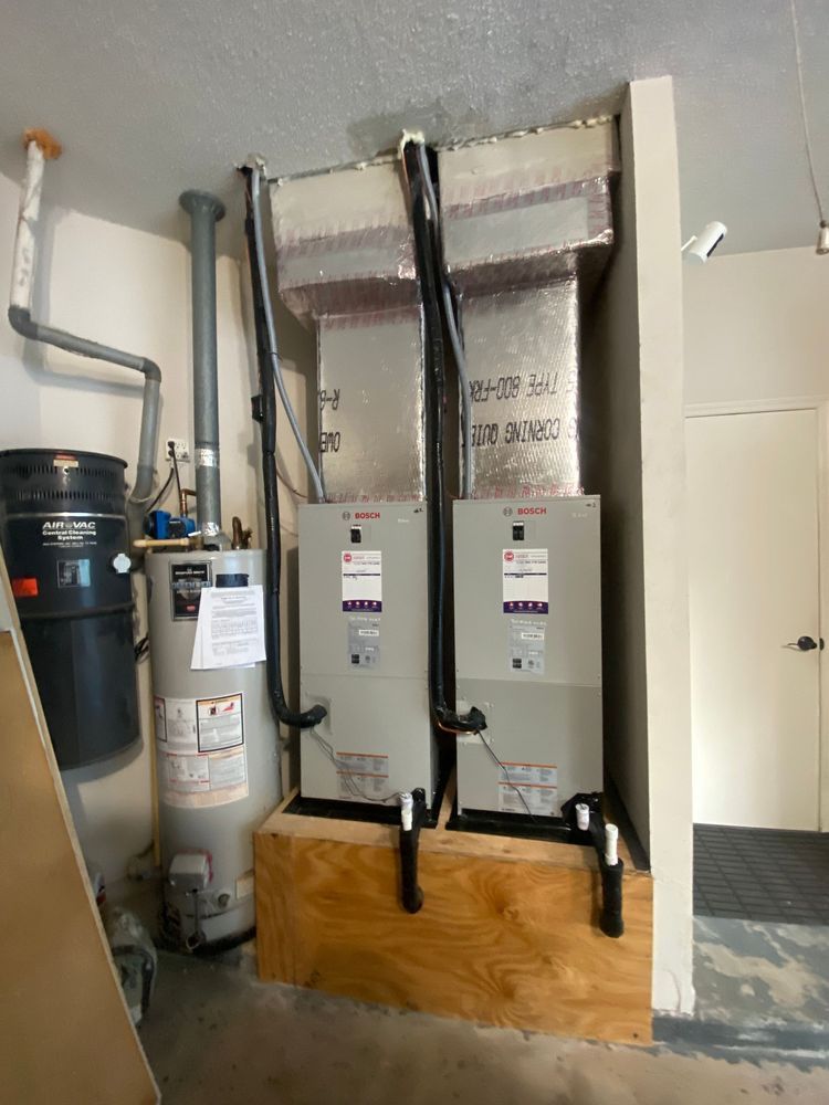 Two HVAC units and a water heater on a wooden platform in a utility room.