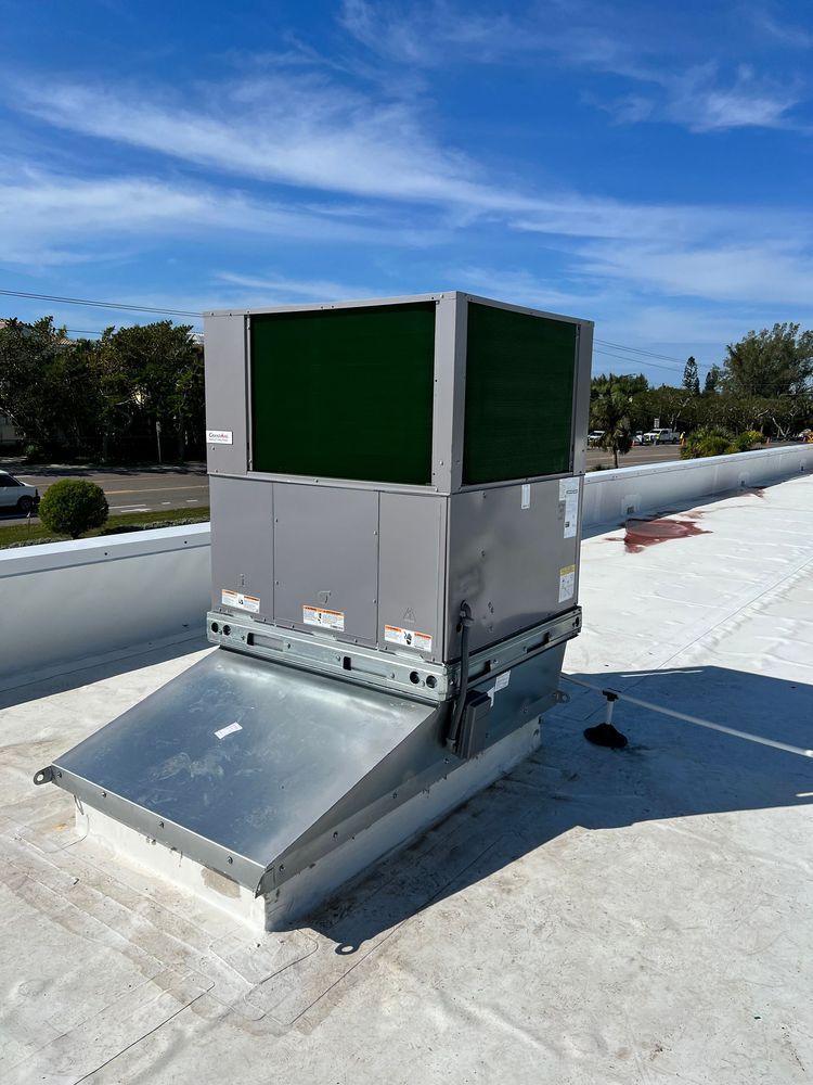 HVAC unit on a rooftop with a blue sky background. The unit is silver and has green cooling pads.