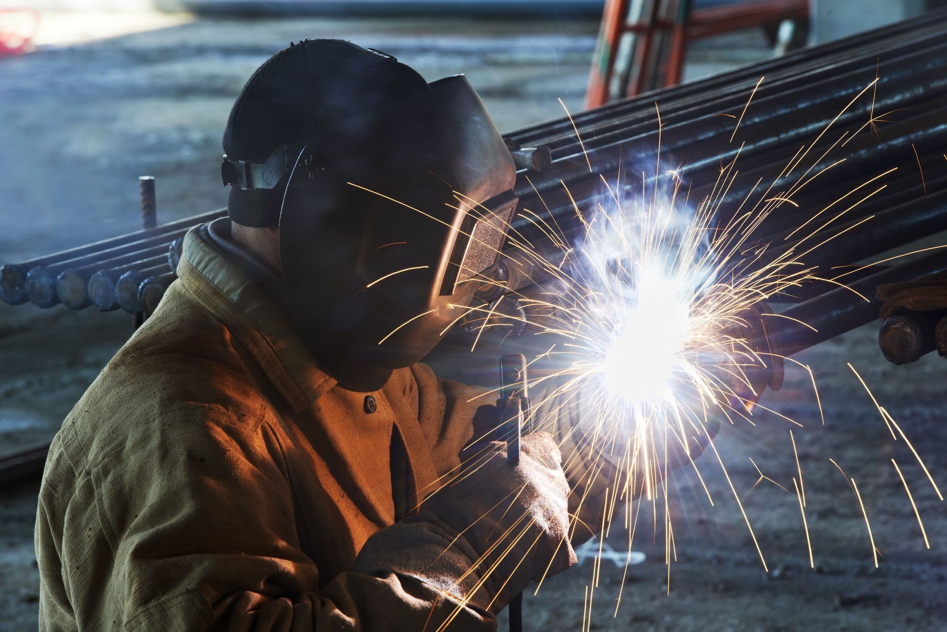 Welder in a protective mask, welding metal rods with bright sparks.