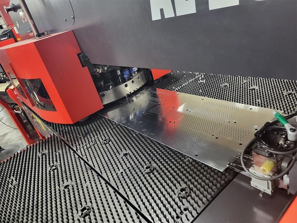 A sheet metal punching machine in action, featuring red and silver components, with a perforated metal sheet on the table.