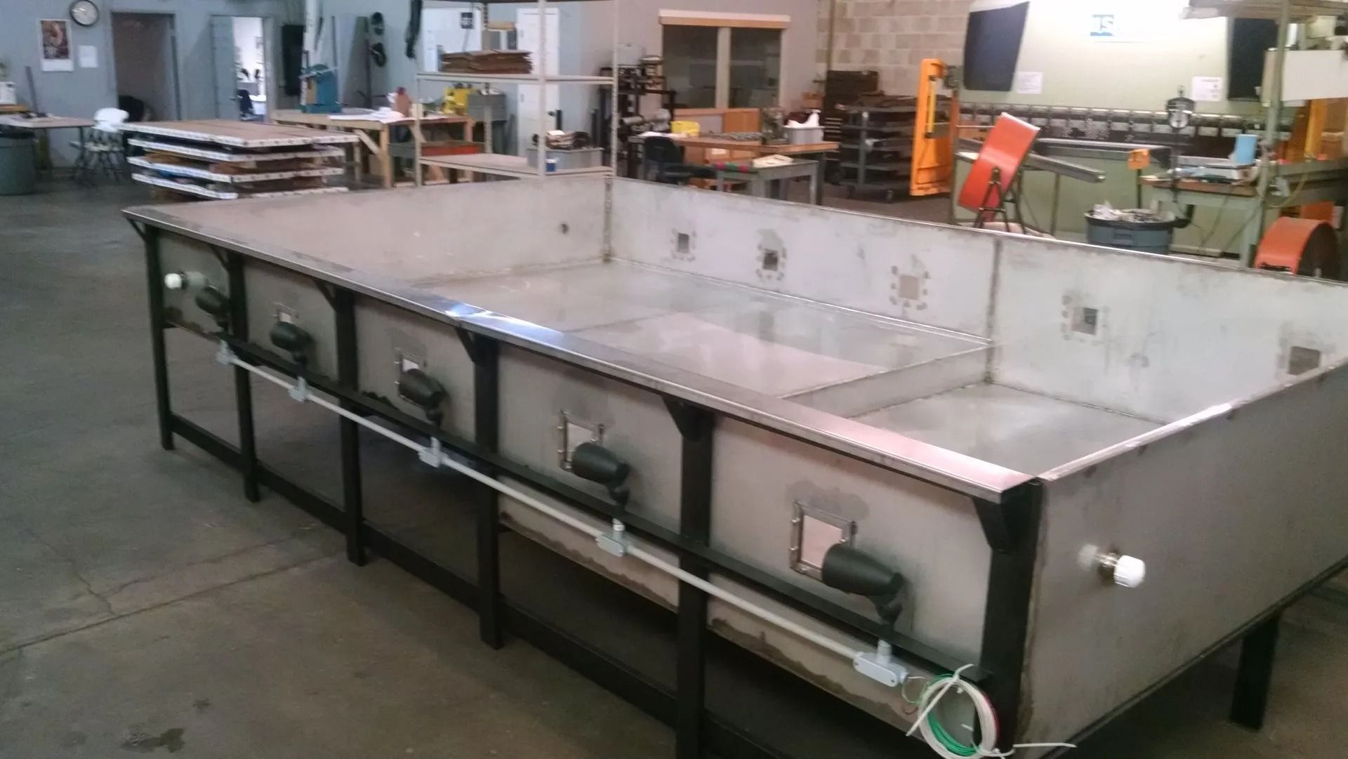 Large, rectangular stainless steel tank on a black metal frame, likely industrial, in a workshop setting.