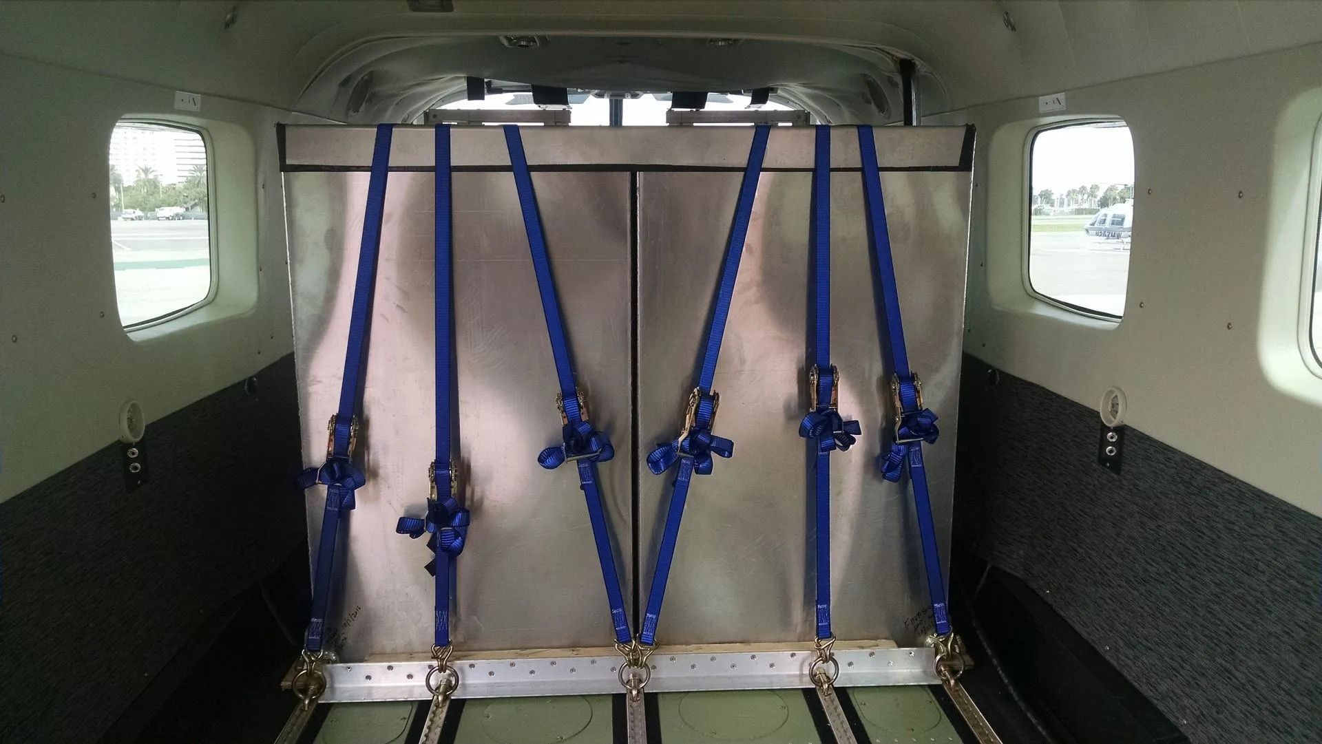 Silver container secured with blue straps inside an aircraft cargo area.