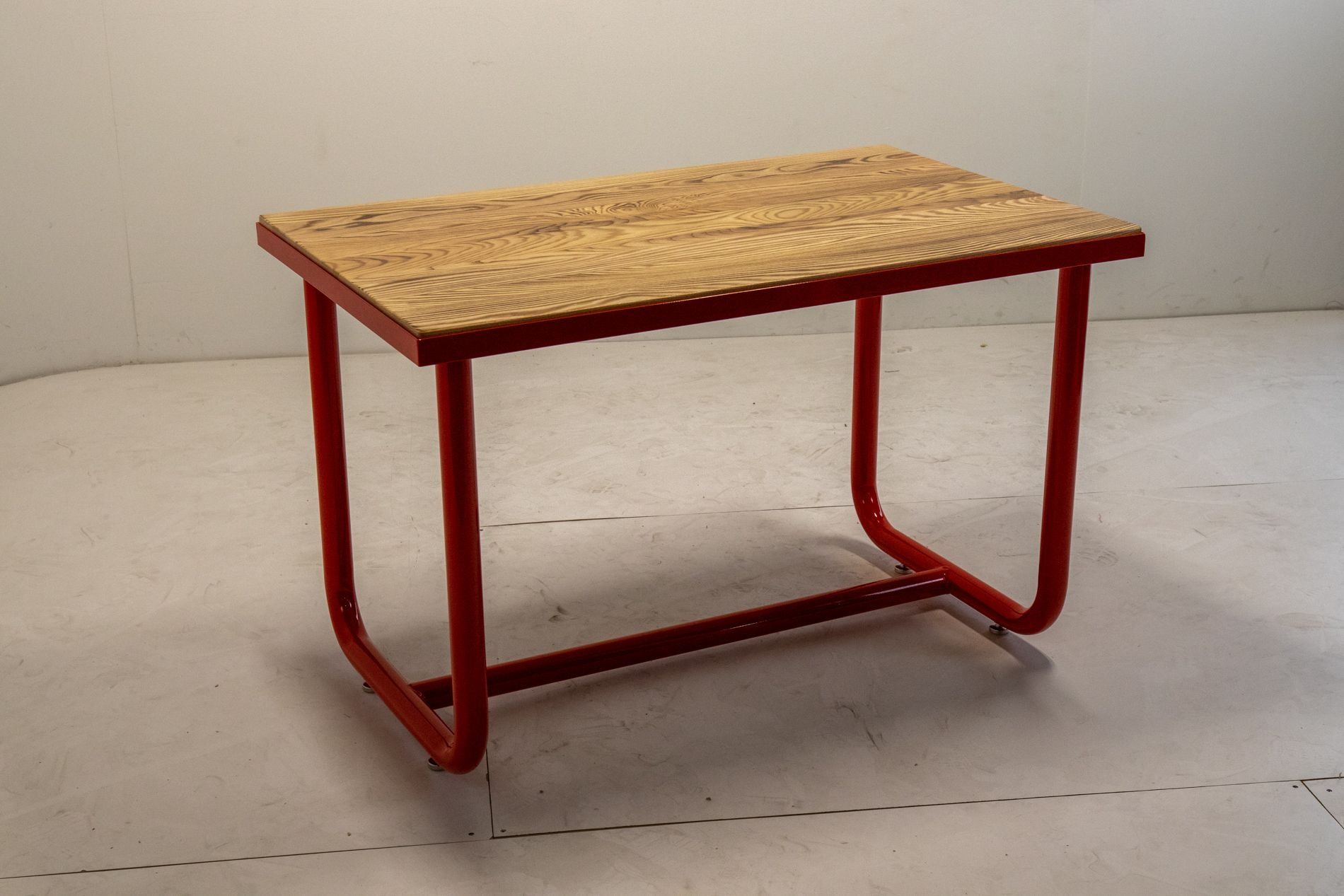 Red metal-framed table with a wood plank top, set against a white wall.