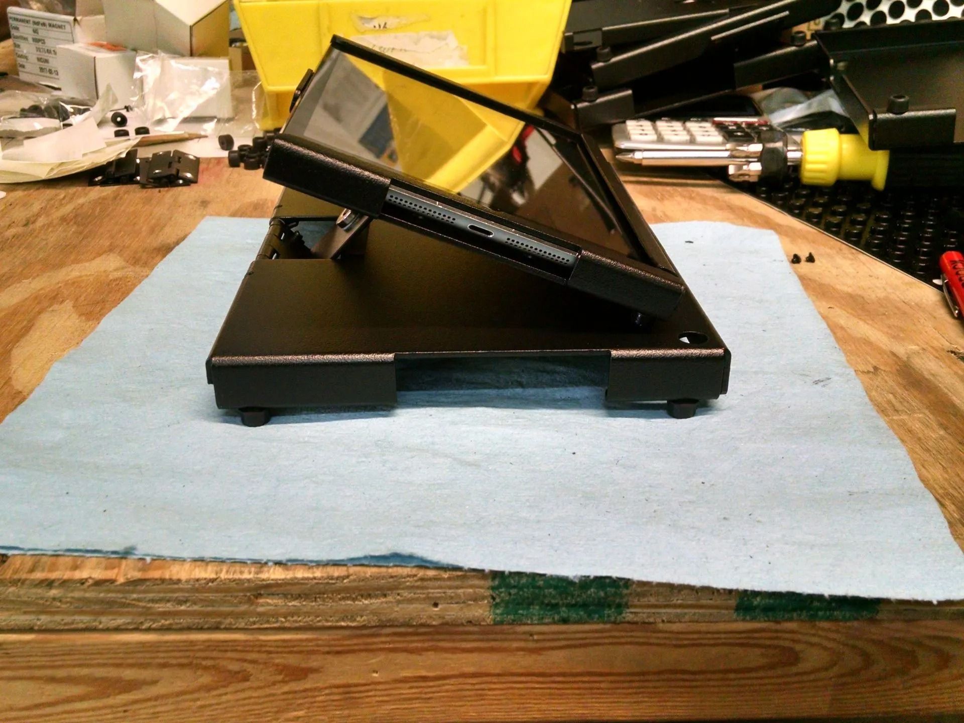 Black electronic device with angled screen on a blue cloth, workbench setting.