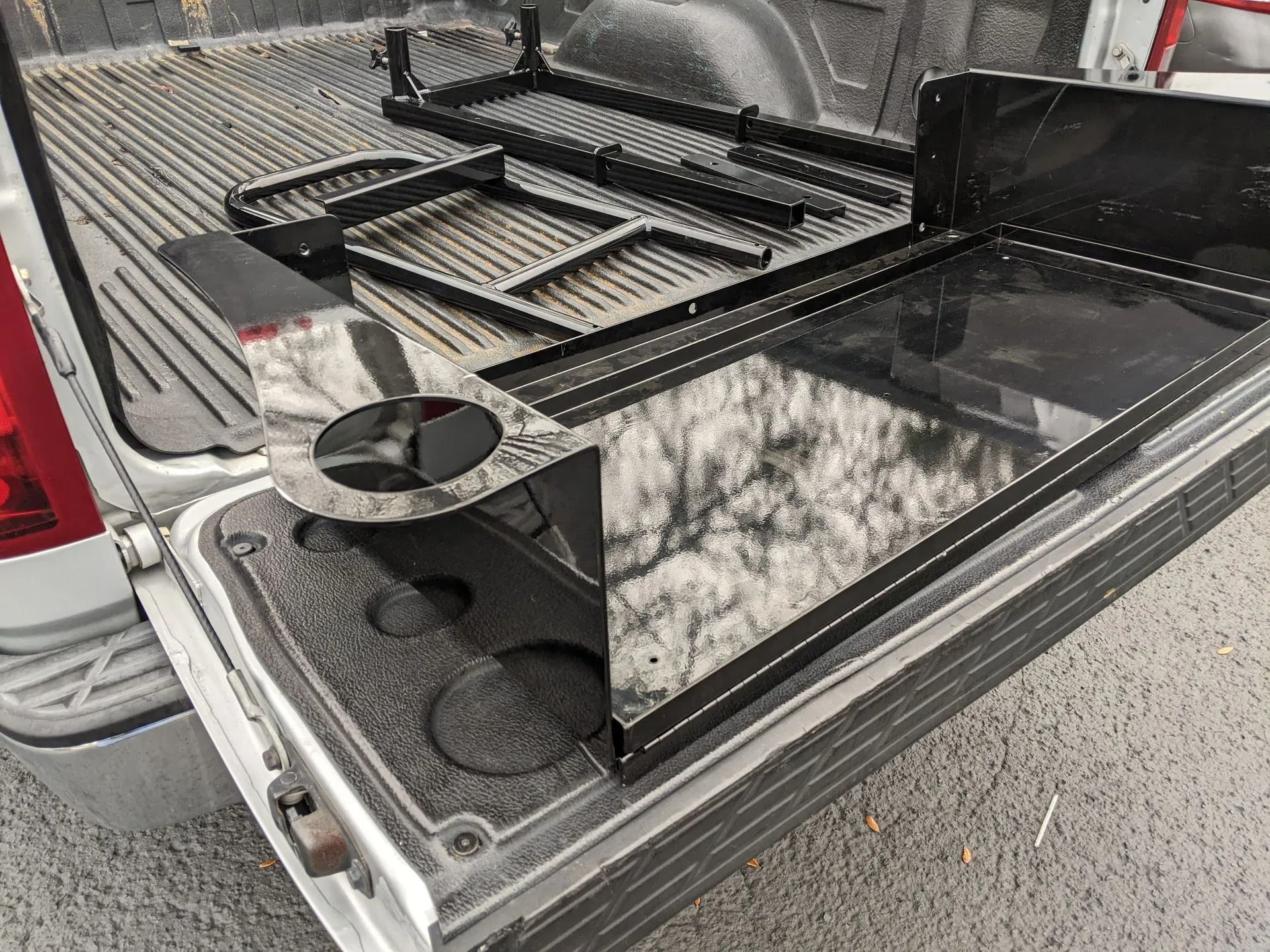 Black metal truck bed accessory with a griddle, shelves, and cupholder.