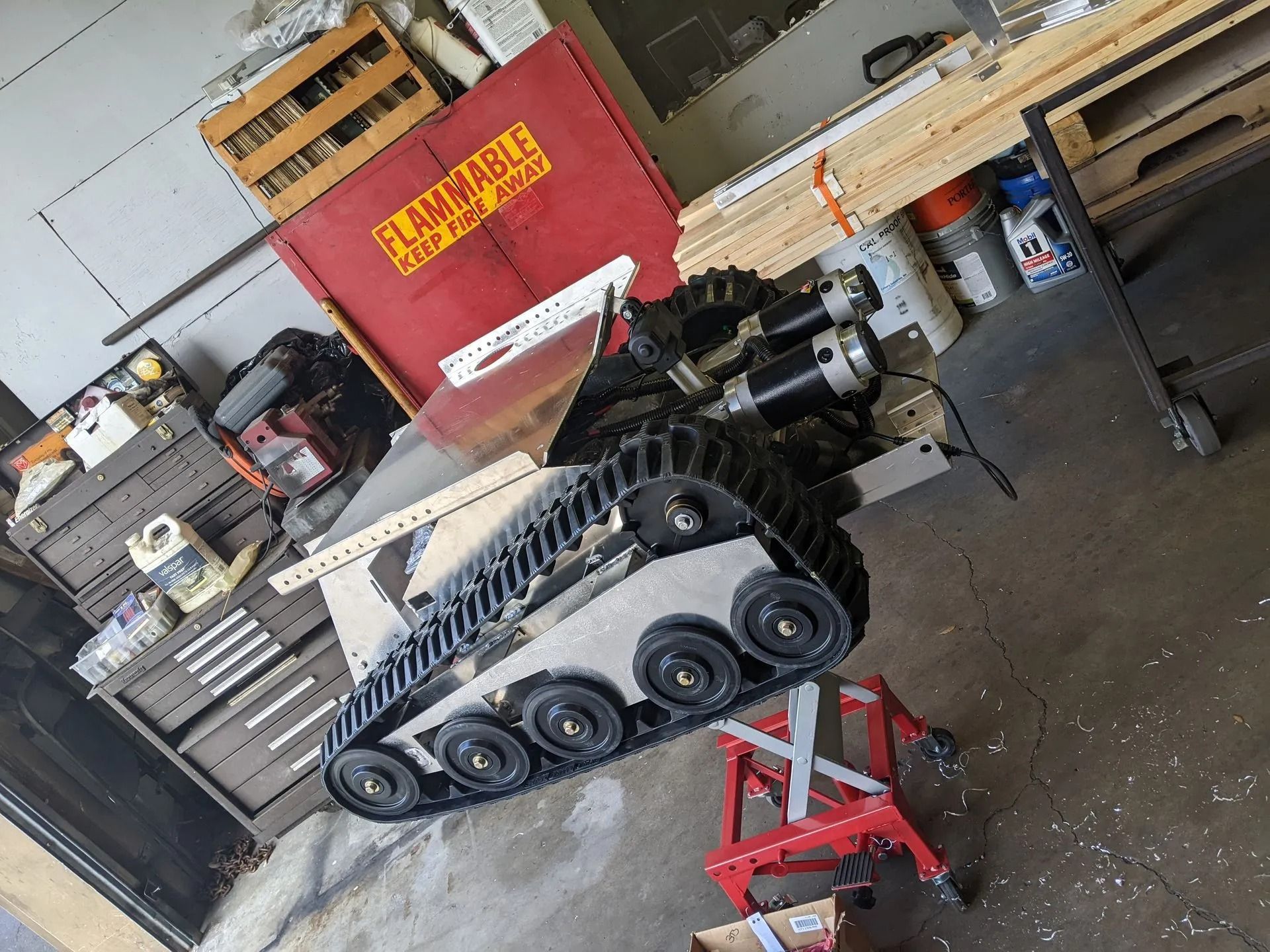 A tracked robot in a workshop. It is supported by a red sawhorse.