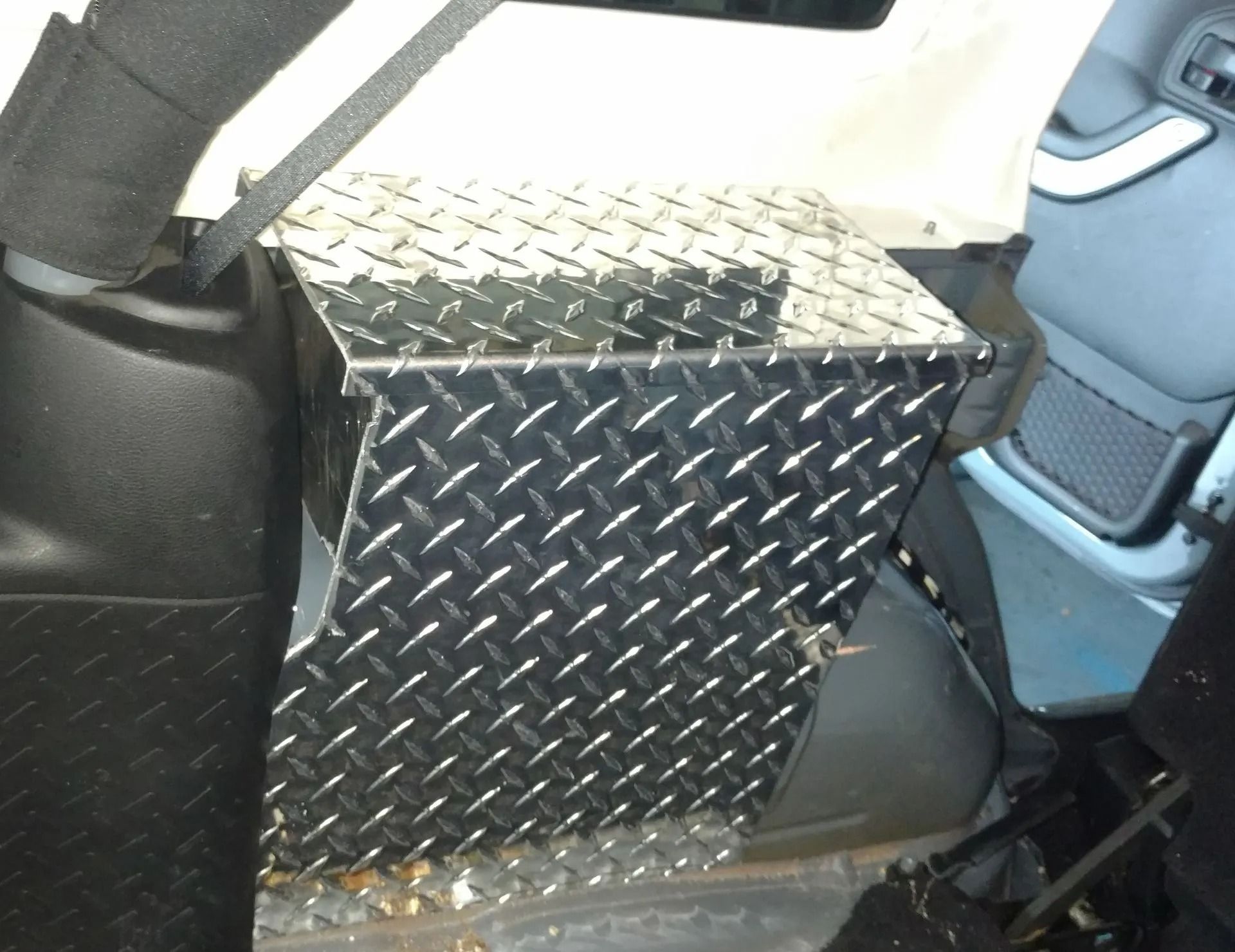 Diamond-plate metal box installed in the back of a light-colored vehicle, likely for storage or protection.