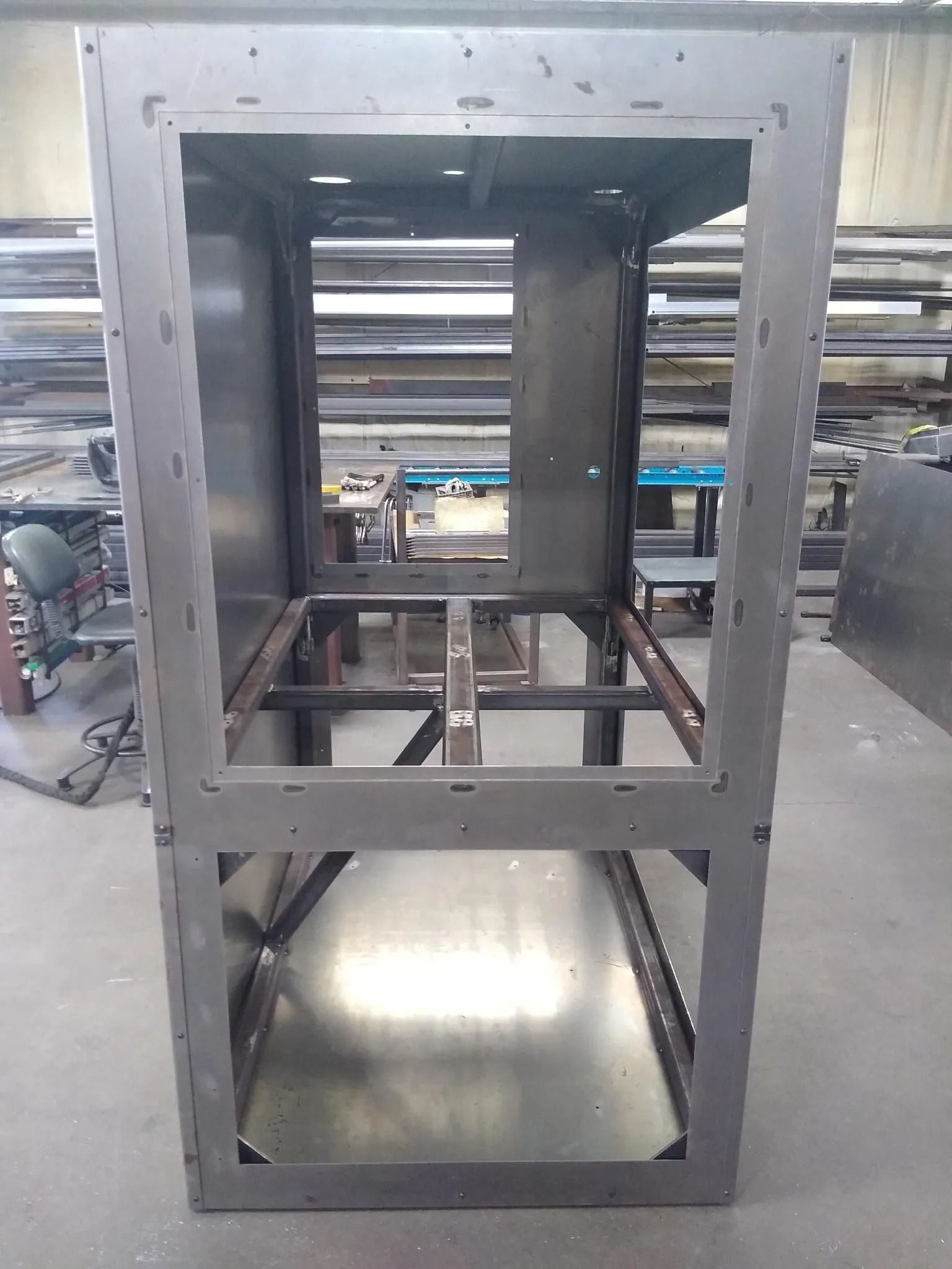 Metal cabinet frame in workshop, with open top, bottom, and center.