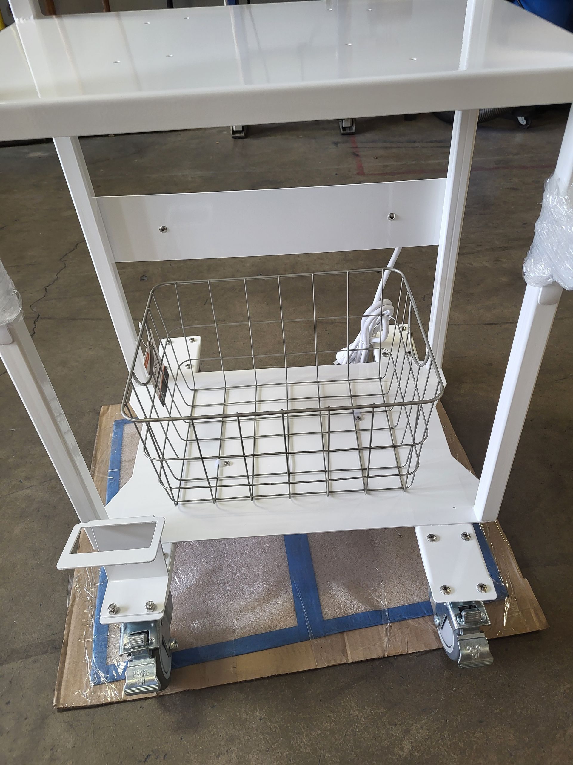 White cart with wire basket, wheels, on a cardboard base.