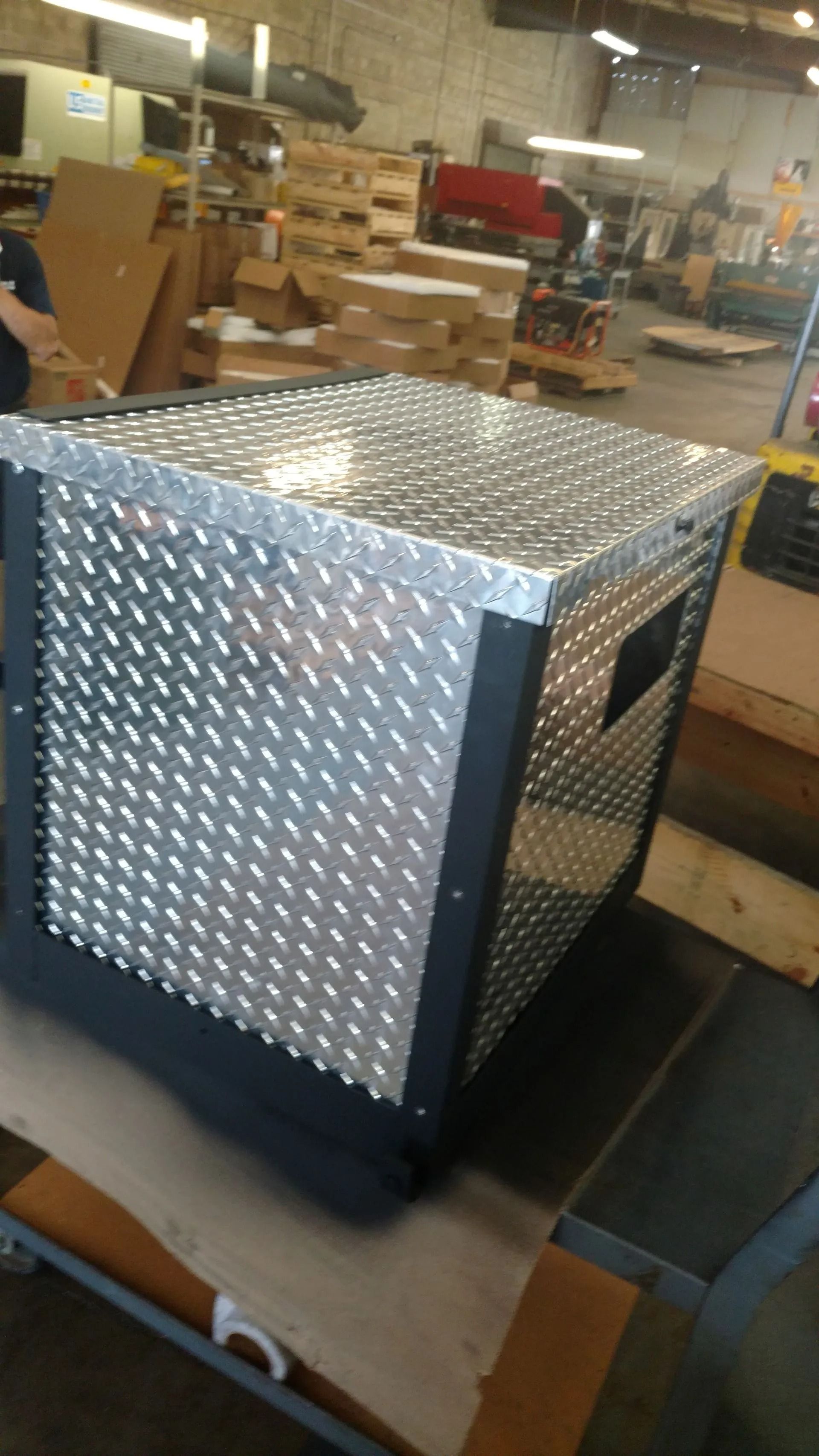 Diamond-plate metal box with a black frame, inside a warehouse.
