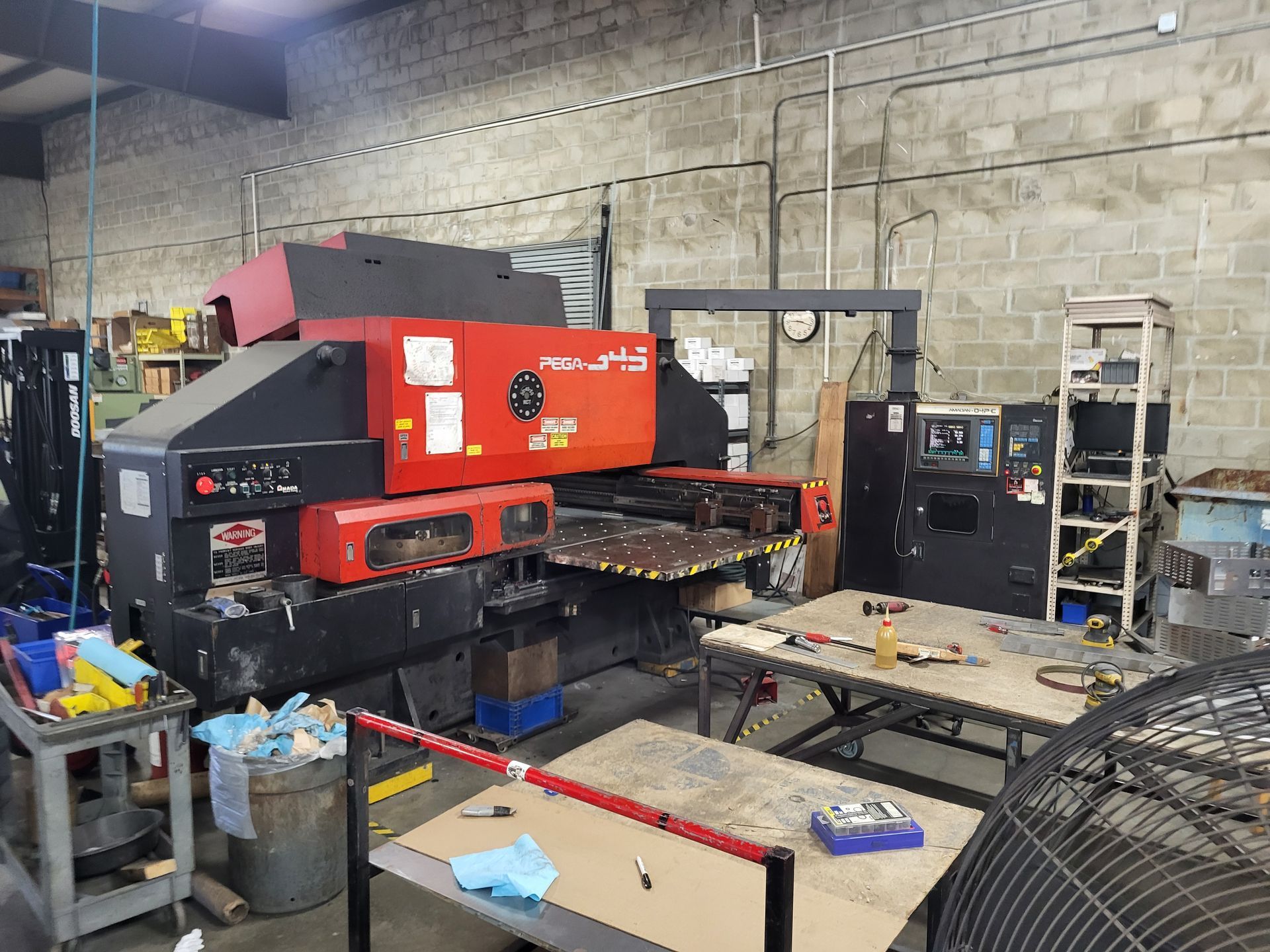 Large industrial punching machine in a workshop. Red and black, with nearby tools and a worktable.