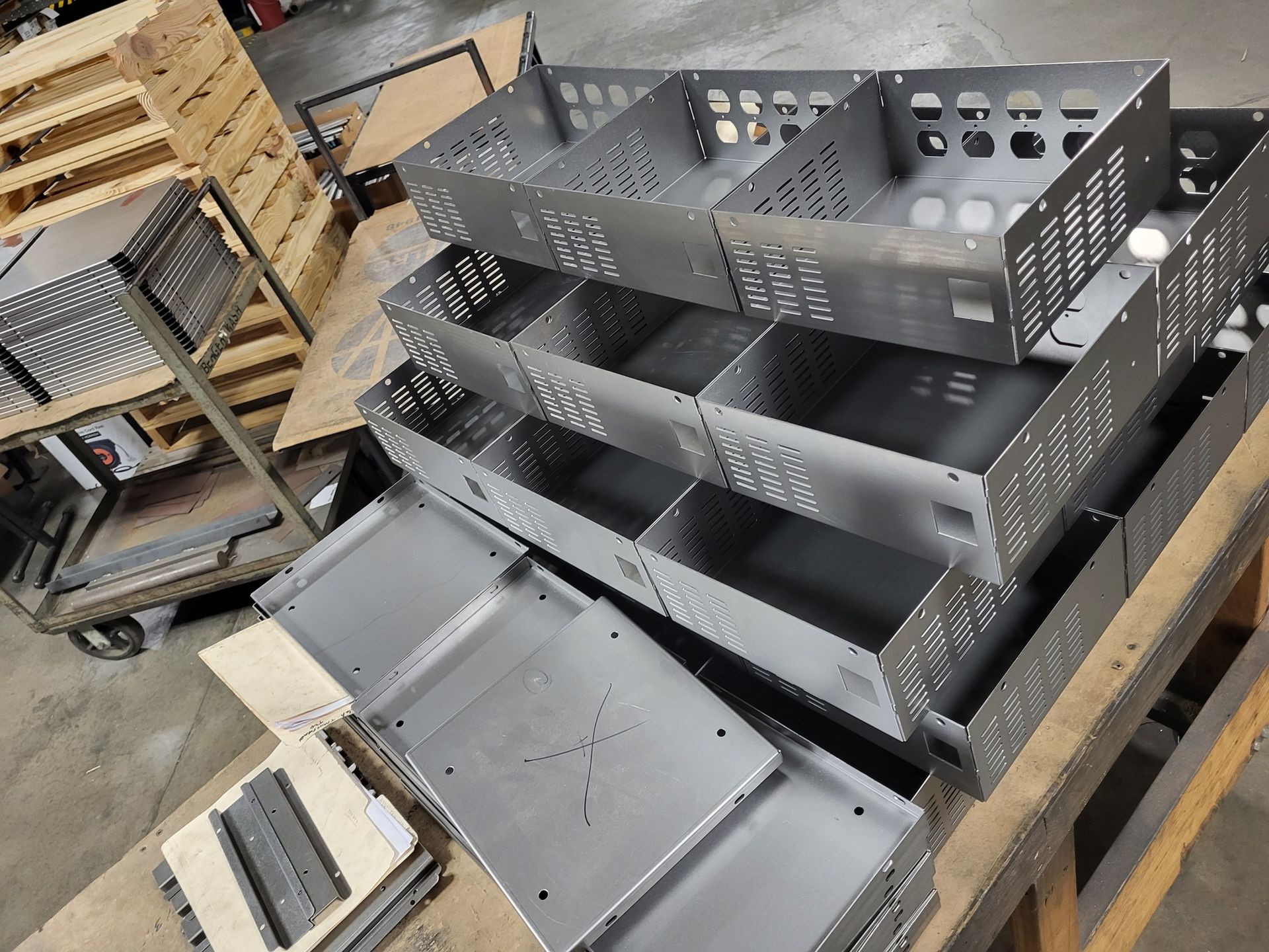 Stack of silver metal storage bins with dividers, on a wooden pallet in a factory.