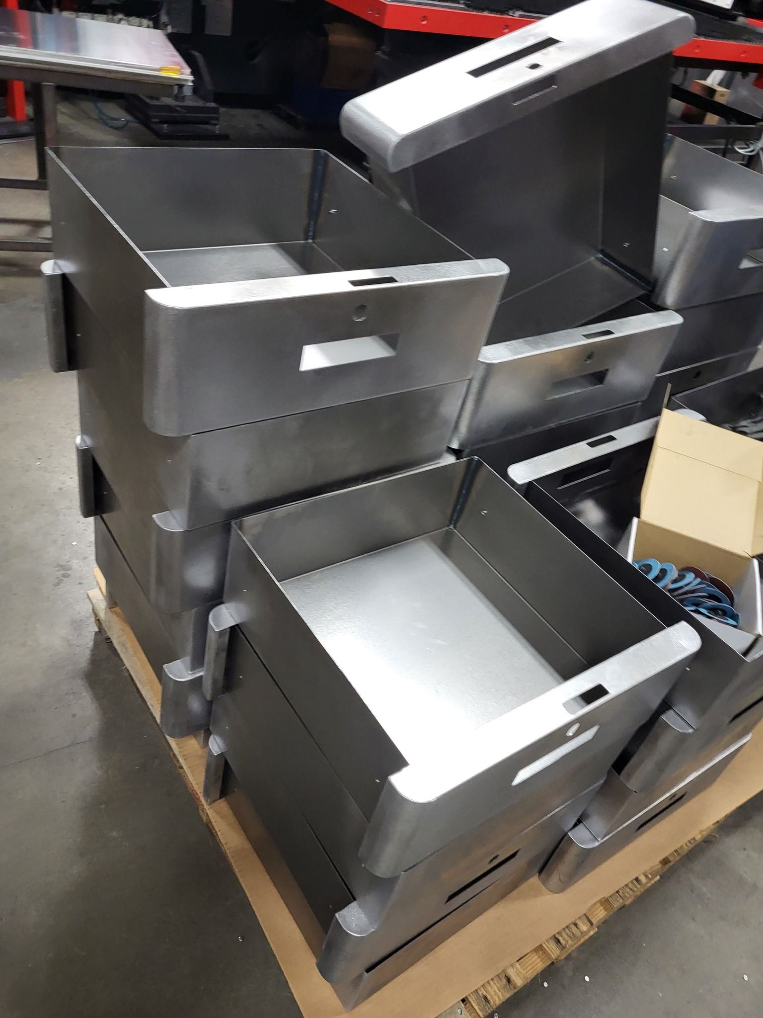 Stacked metal storage bins with handles and slots. Industrial setting.