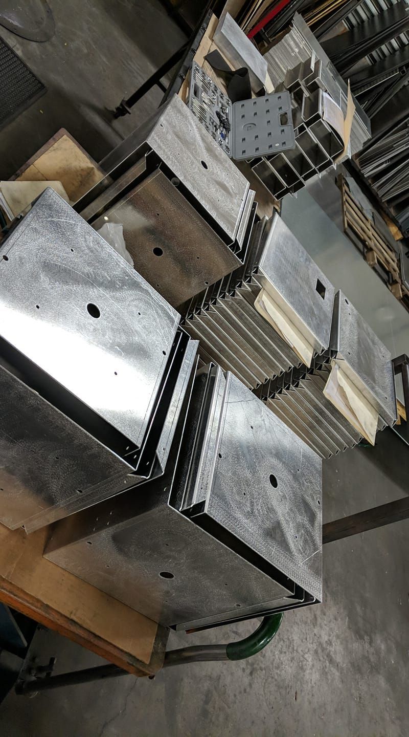 Stacks of metal components, possibly for construction, on a wooden base. Shiny, rectangular shapes.