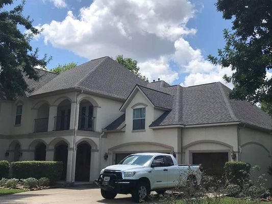 Two-story beige house with a gray roof and a white pickup truck parked in front on a sunny day.