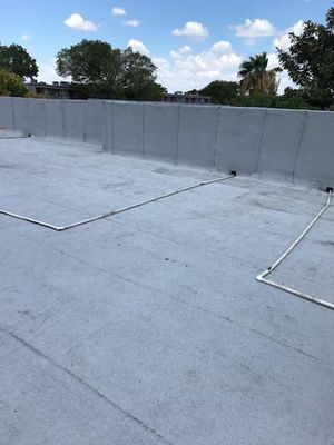 A flat, gray rooftop with white piping. A gray wall surrounds the roof, with a bright blue sky above.
