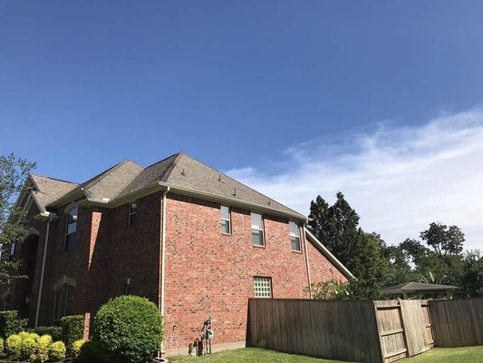 Red brick house with brown roof, set against a blue sky. A wooden fence runs along the side.