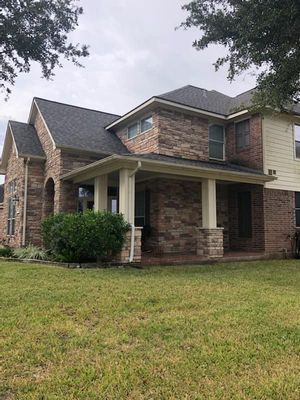 Two-story brick house with a covered porch and a green lawn on a cloudy day.