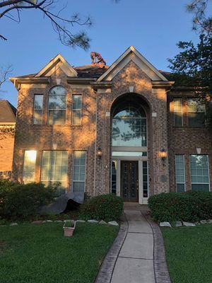 Two-story brick house with a person on the roof, a walkway, and a green lawn.