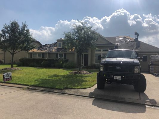 A house with roof shingles being replaced, a truck parked in the driveway, and a blue sky with clouds.