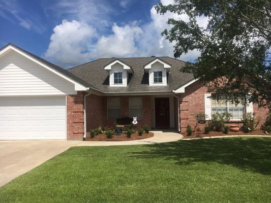 A brick ranch-style house with a white garage door, two dormers, and a green lawn under a blue sky.