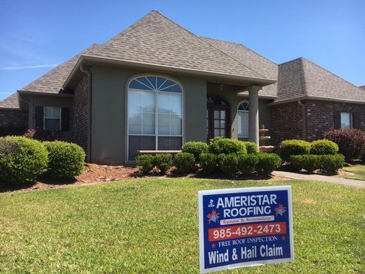 House with a brown roof and green lawn, with a sign for Ameristar Roofing advertising wind & hail claim inspections.