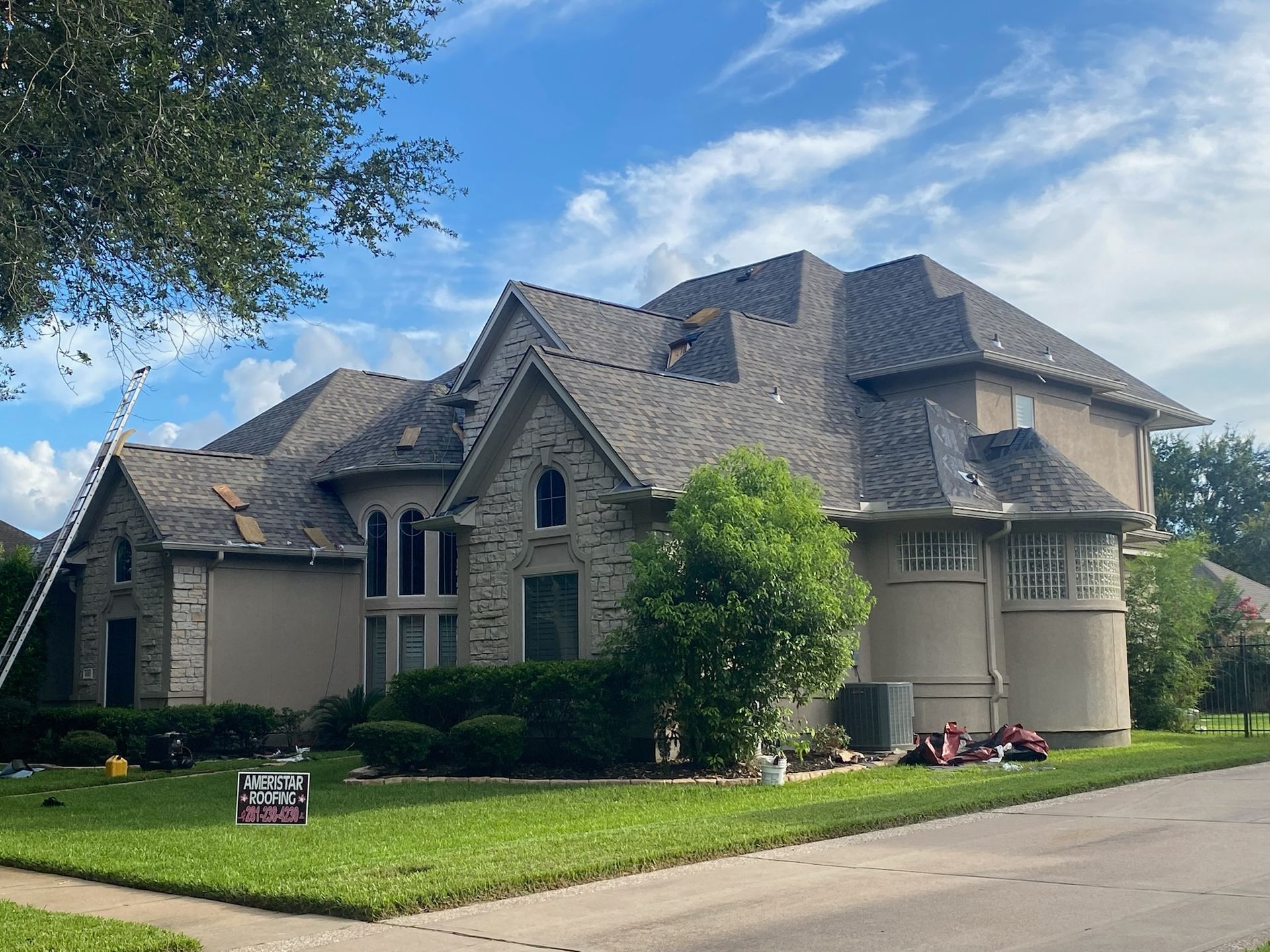 Large two-story house with gray roof, light brick facade, and ladder; a green lawn and blue sky.