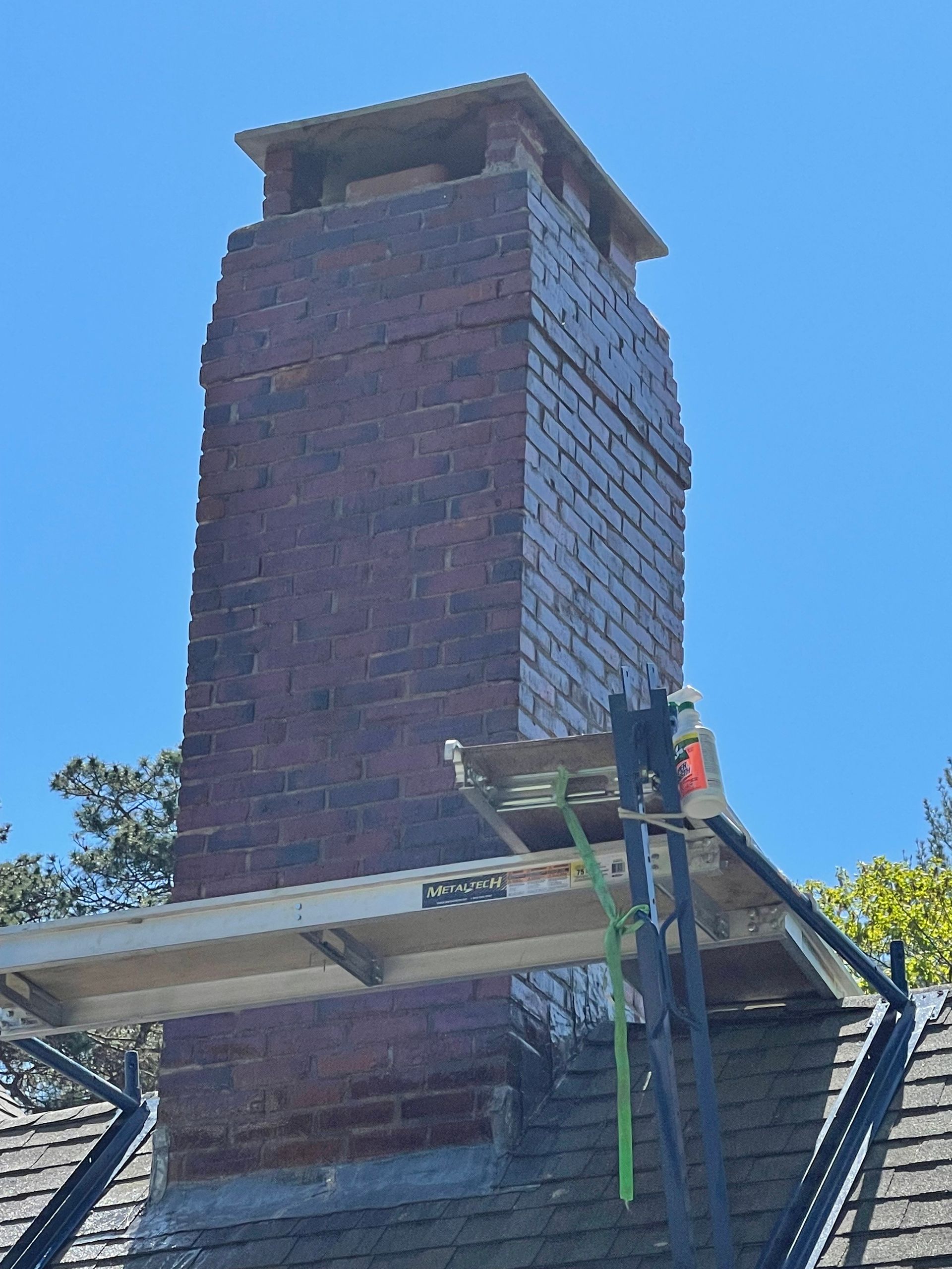 A brick chimney is sitting on top of a roof next to a scaffolding.