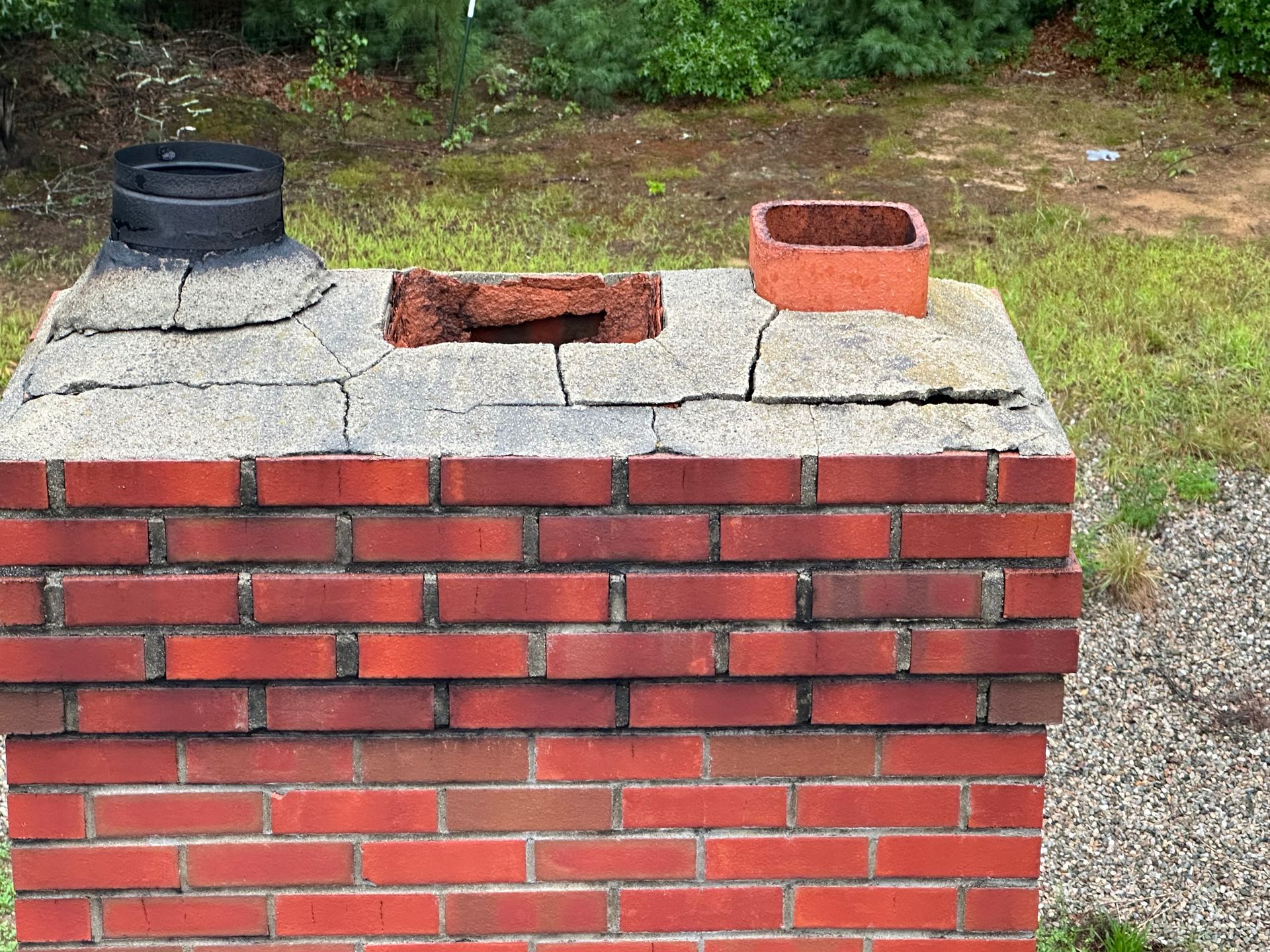 A brick chimney with a hole in it is sitting in the grass.