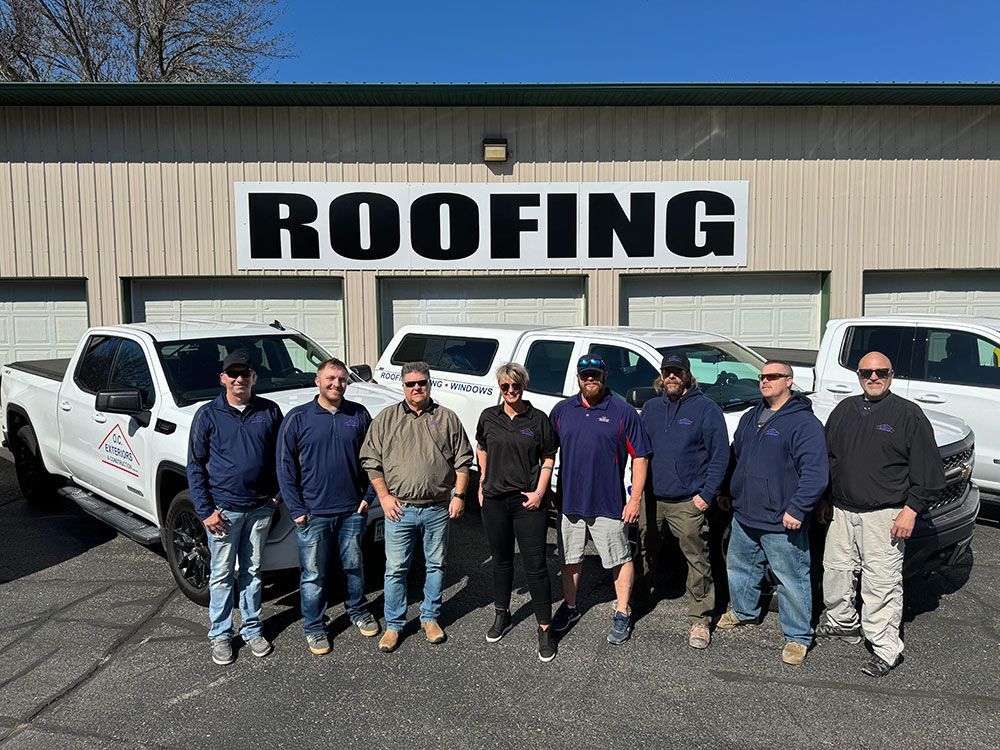 A group of men are posing for a picture in front of a roofing company