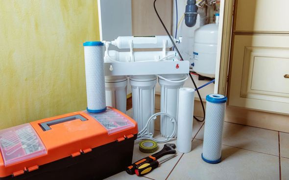 Water filter system with toolbox and tools on the floor next to a cabinet.