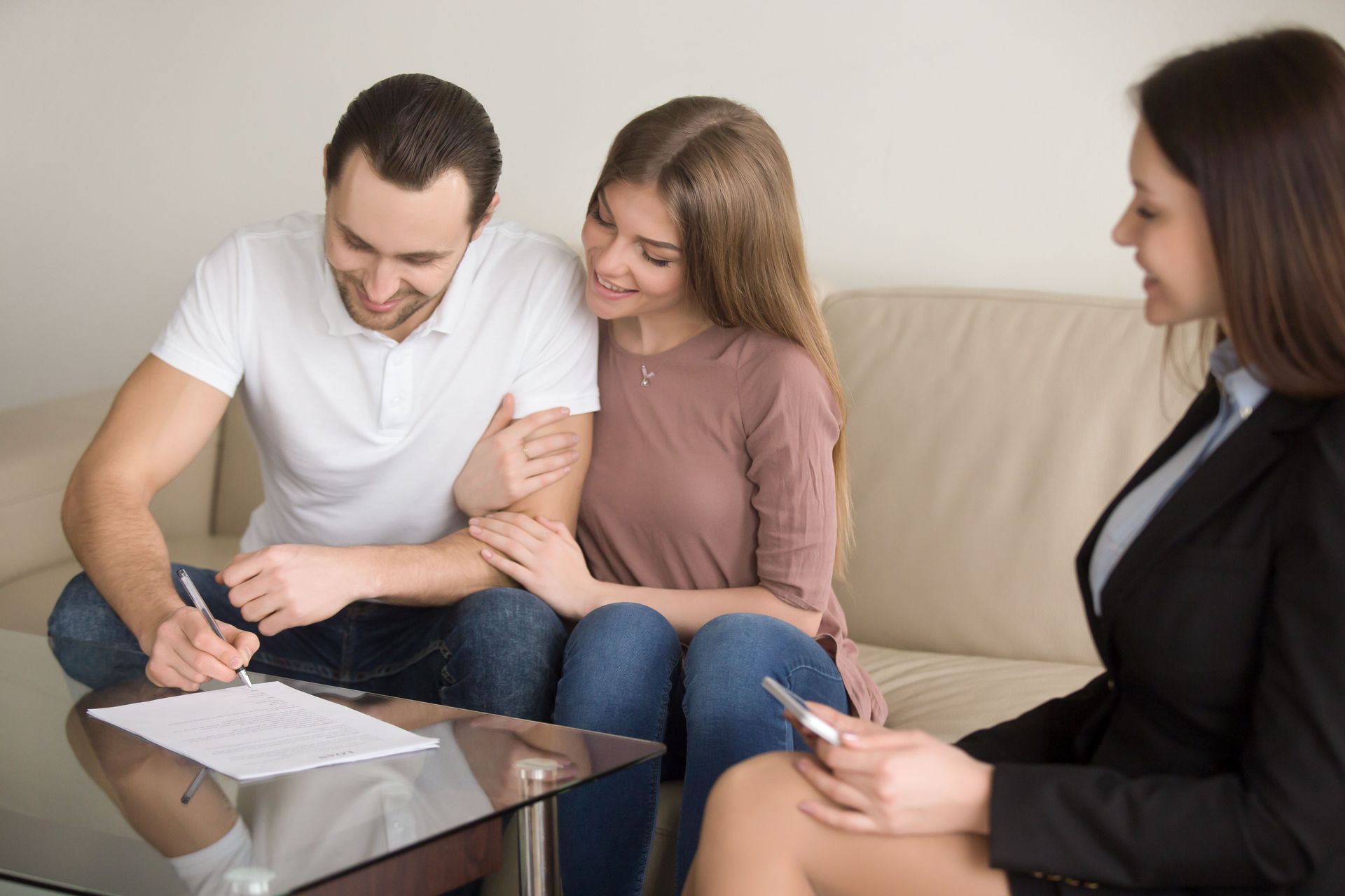 Man signing documents while seated with a woman on a couch and a professional advisor nearby