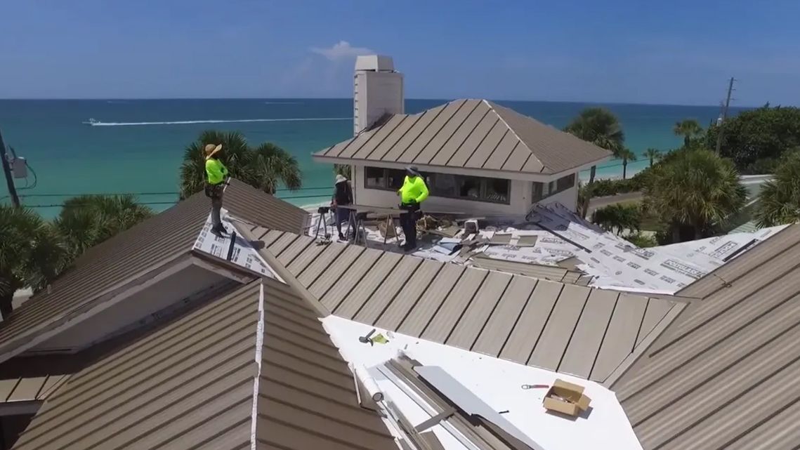 A group of people are working on the roof of a house near the ocean.