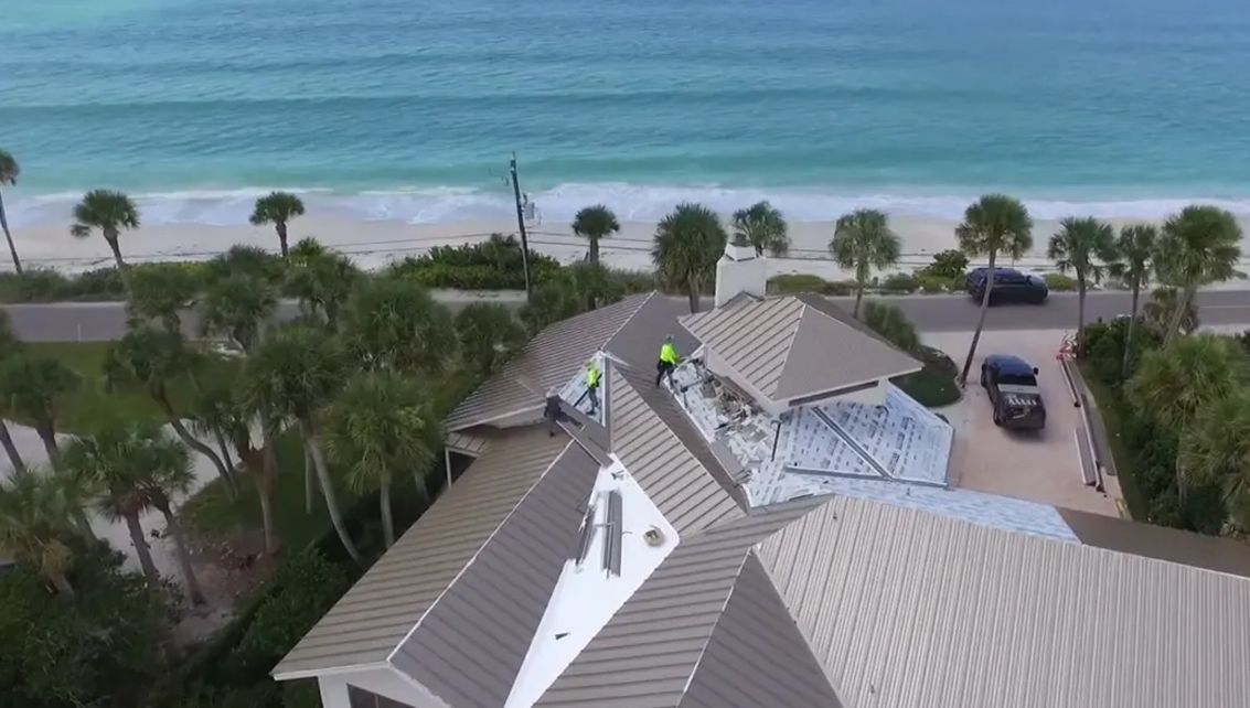 An aerial view of a house with a roof that is being repaired near the ocean.