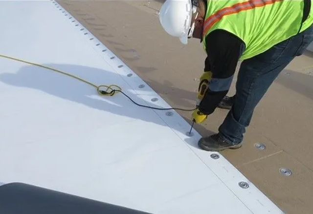 A man wearing a hard hat and safety vest is working on a roof