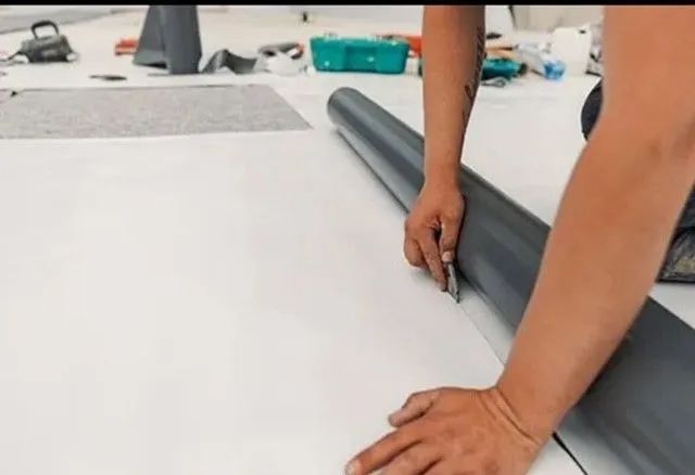 A person is laying a roll of vinyl flooring on the floor.