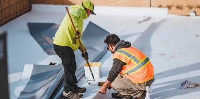 Two construction workers are working on a roof.