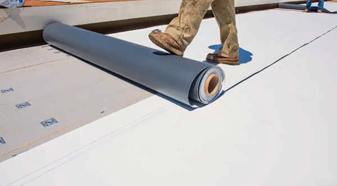 A man is rolling a roll of roofing material on a roof.