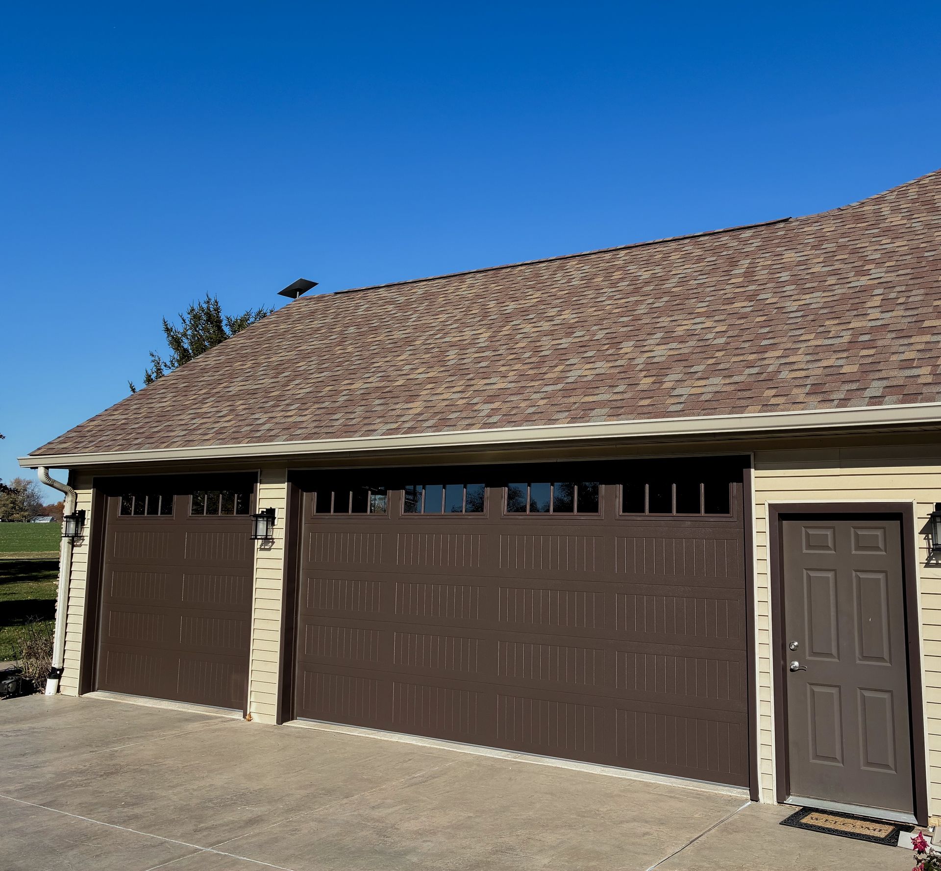 Brown garage doors and a matching door under a brown roof against a blue sky.