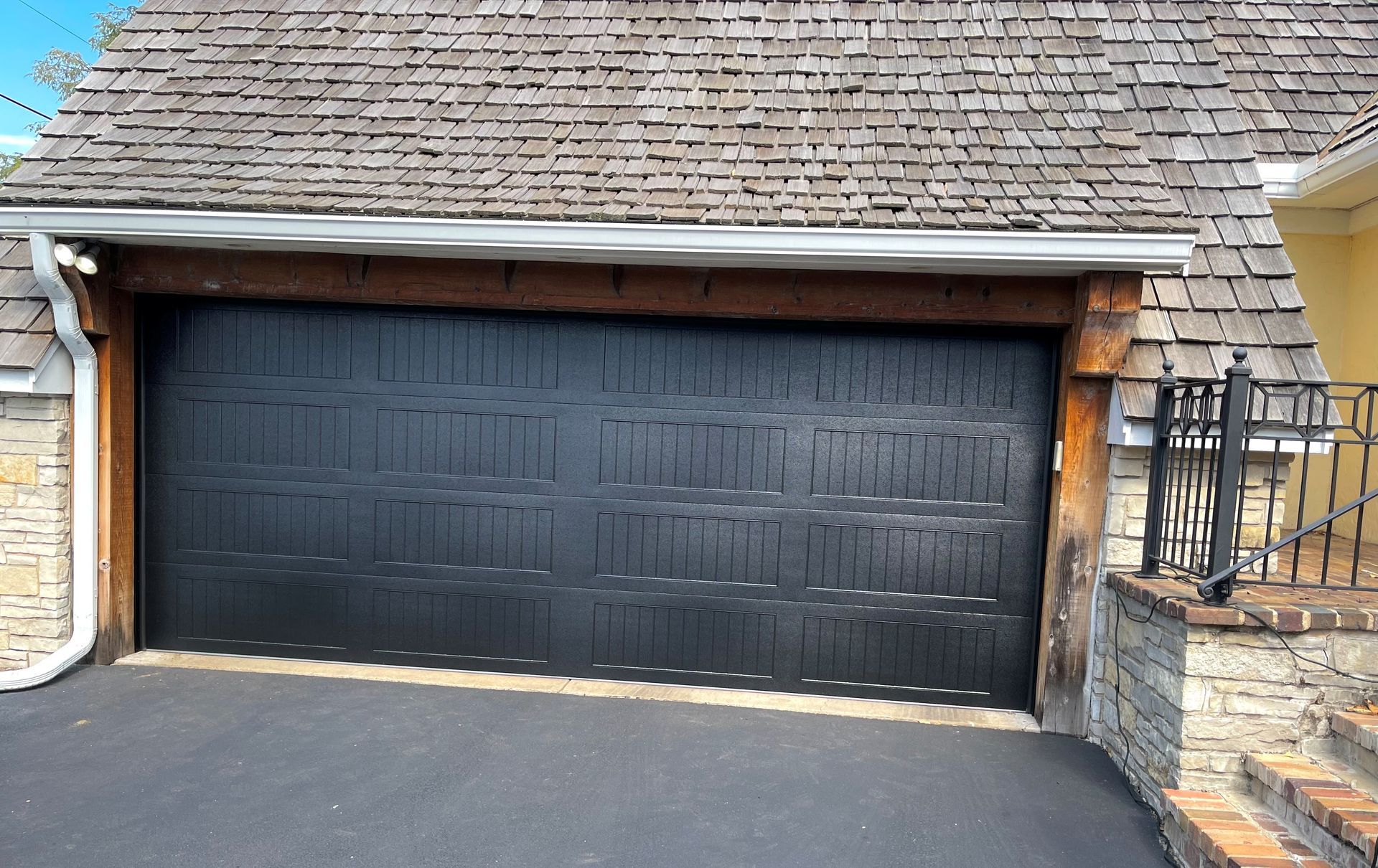 Black garage door under a cedar shake roof; driveway in front.