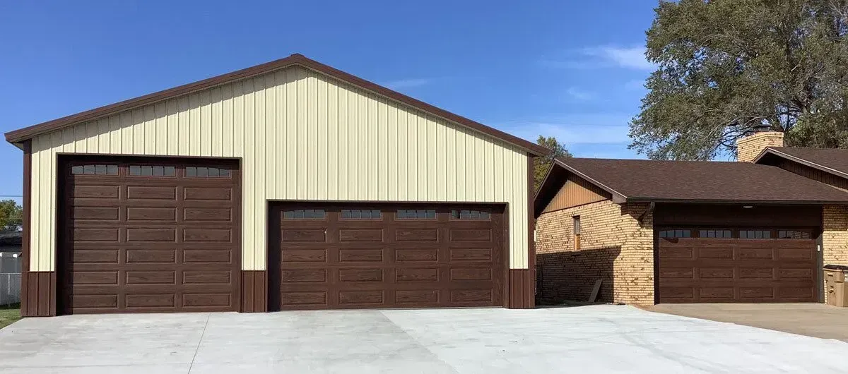 Brown and beige garage doors on a concrete driveway, next to a rock and wood structure. Blue sky.