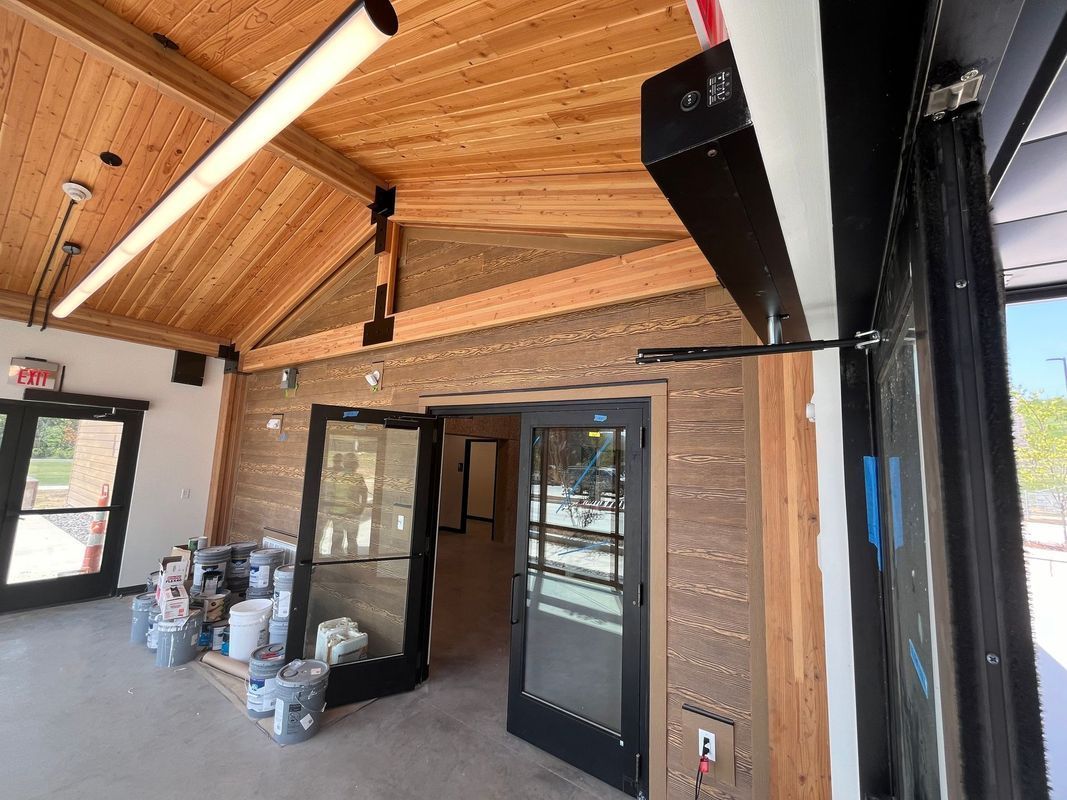 Interior view of a building under construction, featuring wood-paneled walls and ceiling, black door frames, and flooring.