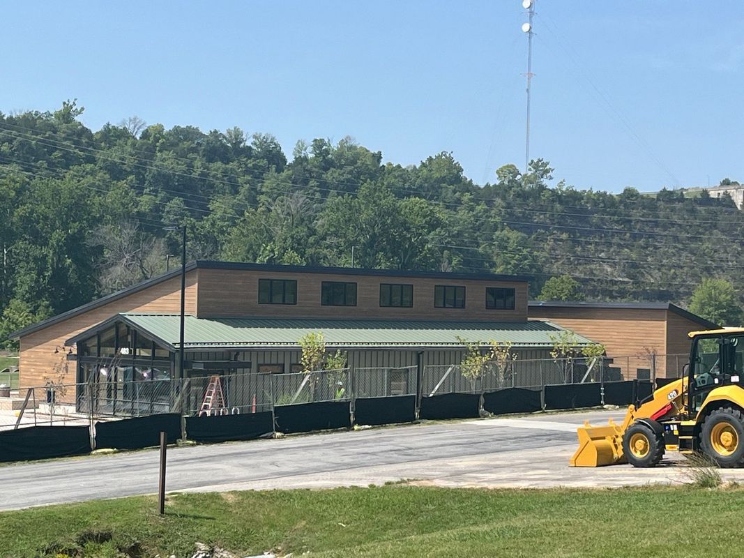 A modern wooden building under construction, surrounded by a black fence, with a yellow tractor parked in front.