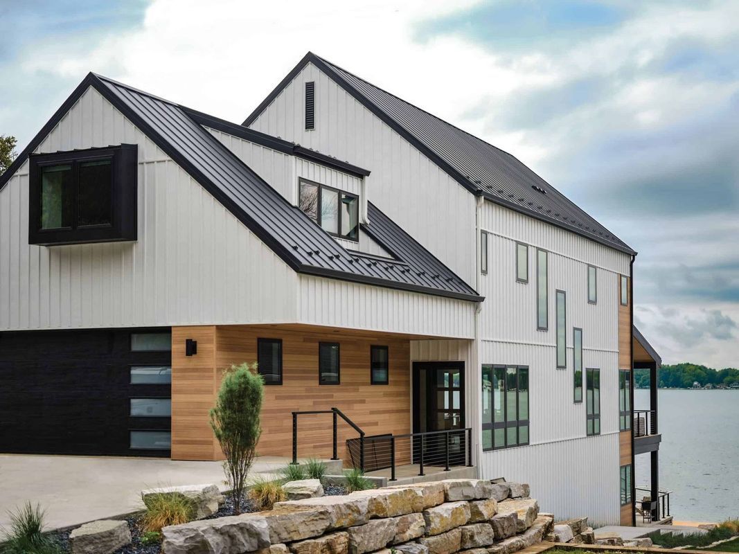 Modern, multi-level lakefront home with white vertical siding, dark metal roof, wood accents, and a black garage.