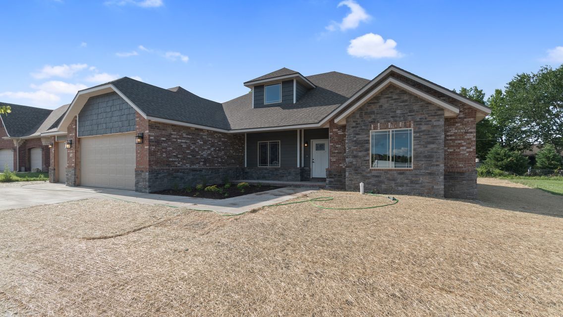 A suburban house with a brick and stone facade, a multi-car garage, and a large, unfinished yard under a blue sky.