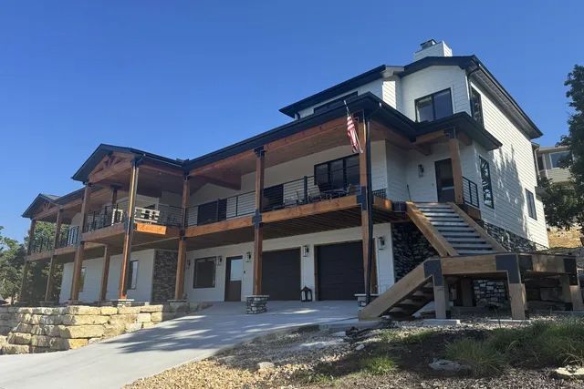 After view of a large modern house with stone lower walls, wooden balconies, and an exterior staircase under a blue sky