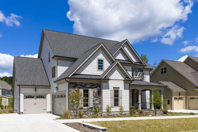 A two-story suburban house with stone and light siding, a gabled roof, and a multi-car garage under a blue sky.
