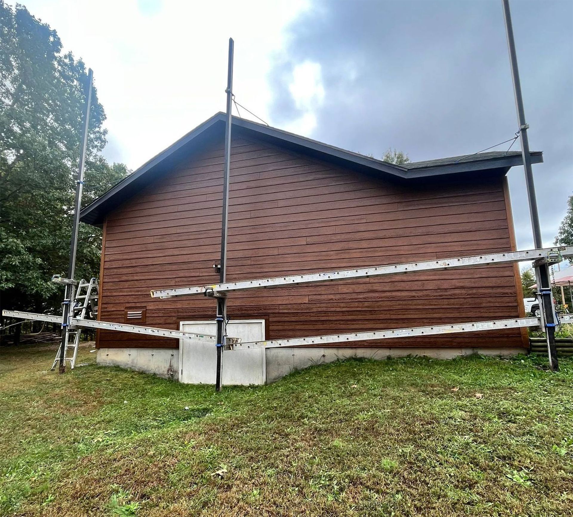 A side view of a brown wooden house with scaffolding poles and boards set up against the exterior wall.