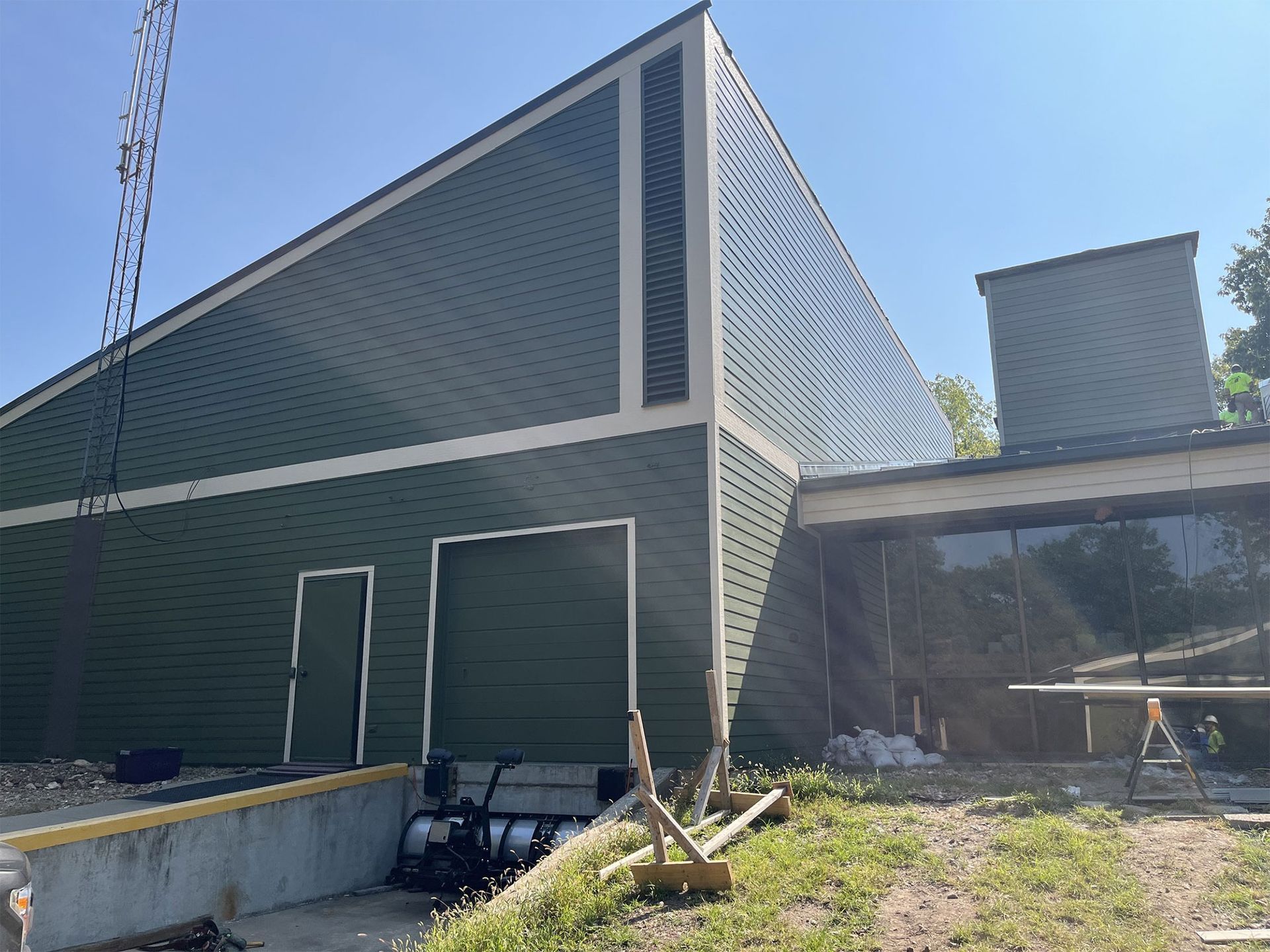 Green modern building with an angled roof and dark glass entrance, adjacent to a loading dock under a clear blue sky.